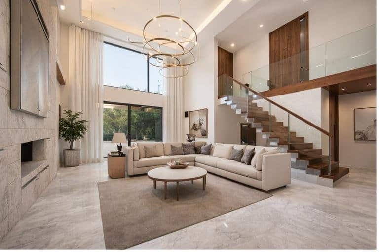 Sala de doble altura con pisos de mármol en acabado brillante, ventanales amplios que permiten entrada de luz natural y diseño contemporáneo con iluminación cálida.